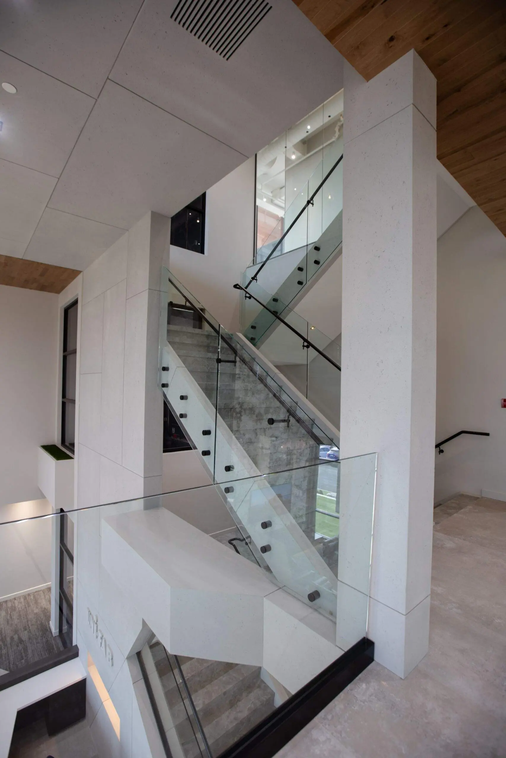 A modern industrial stairway with glass railings, concrete stairs, lightweight concrete cladding, concrete pillar and a wooden ceiling.