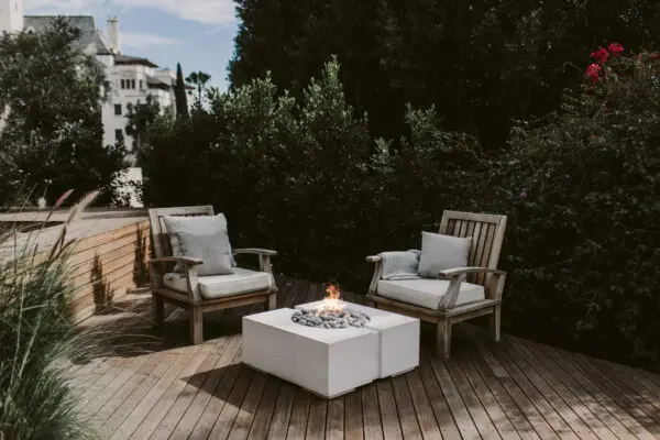 Green garden with a wooden deck in the middle. Two outdoor chairs surround a concrete fire pit.