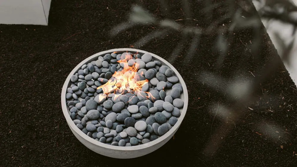 Circular lit concrete fire pit sitting in a garden.