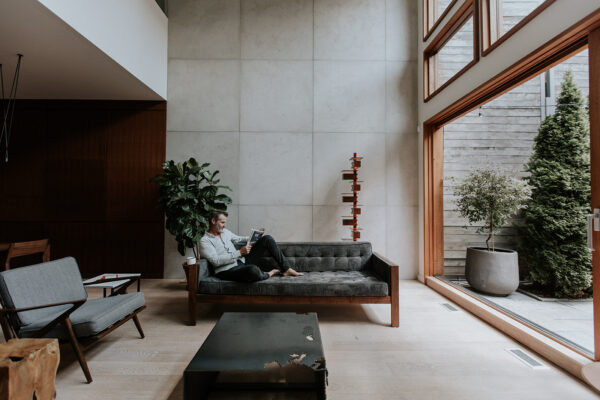 Stylish, modern living space designed with concrete cladding. Middle-aged man on a couch reading.