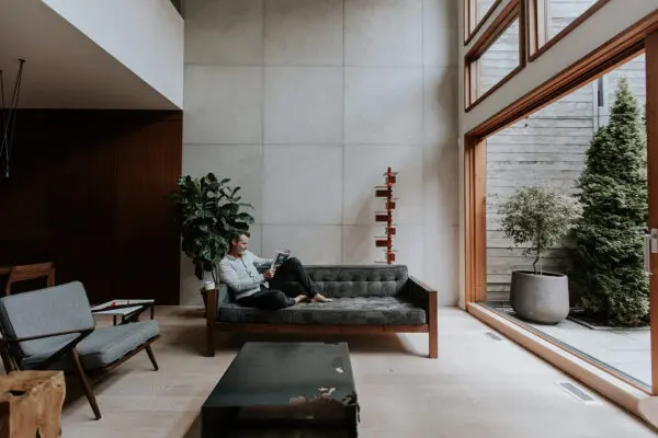 Stylish, modern living space designed with concrete cladding. Middle-aged man on a couch reading.