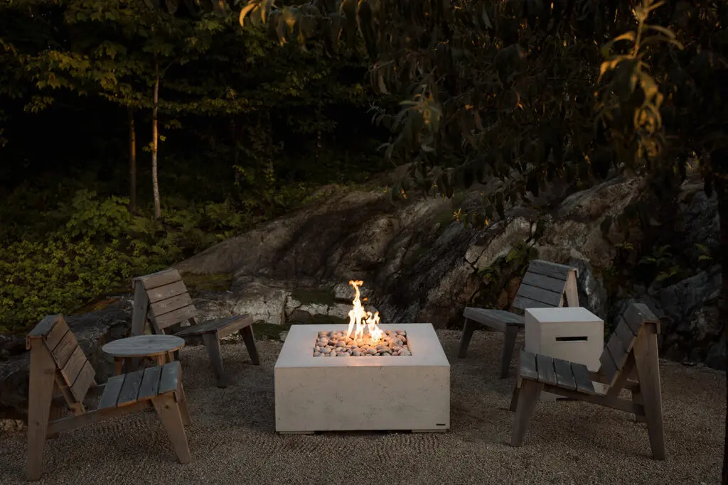 Modern concrete fire pit surrounded by empty lawn furniture. 