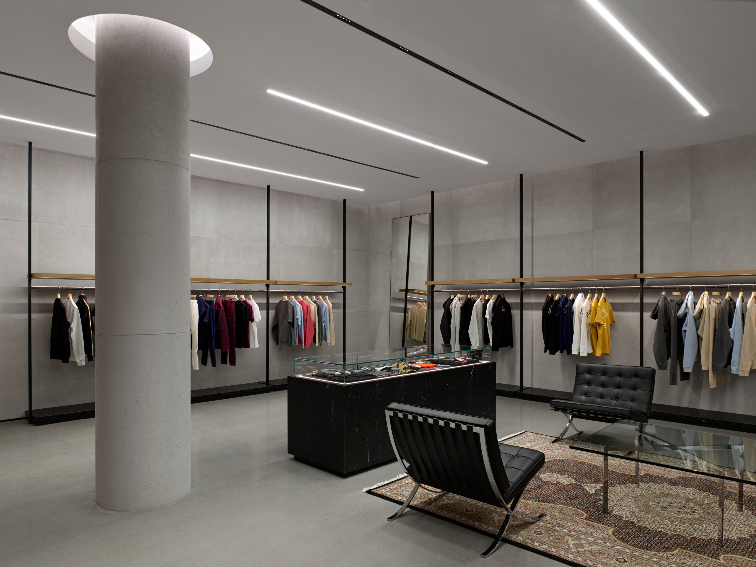 Modern retail space, concrete cladding, concrete pillar with clothing displays and seating area. 