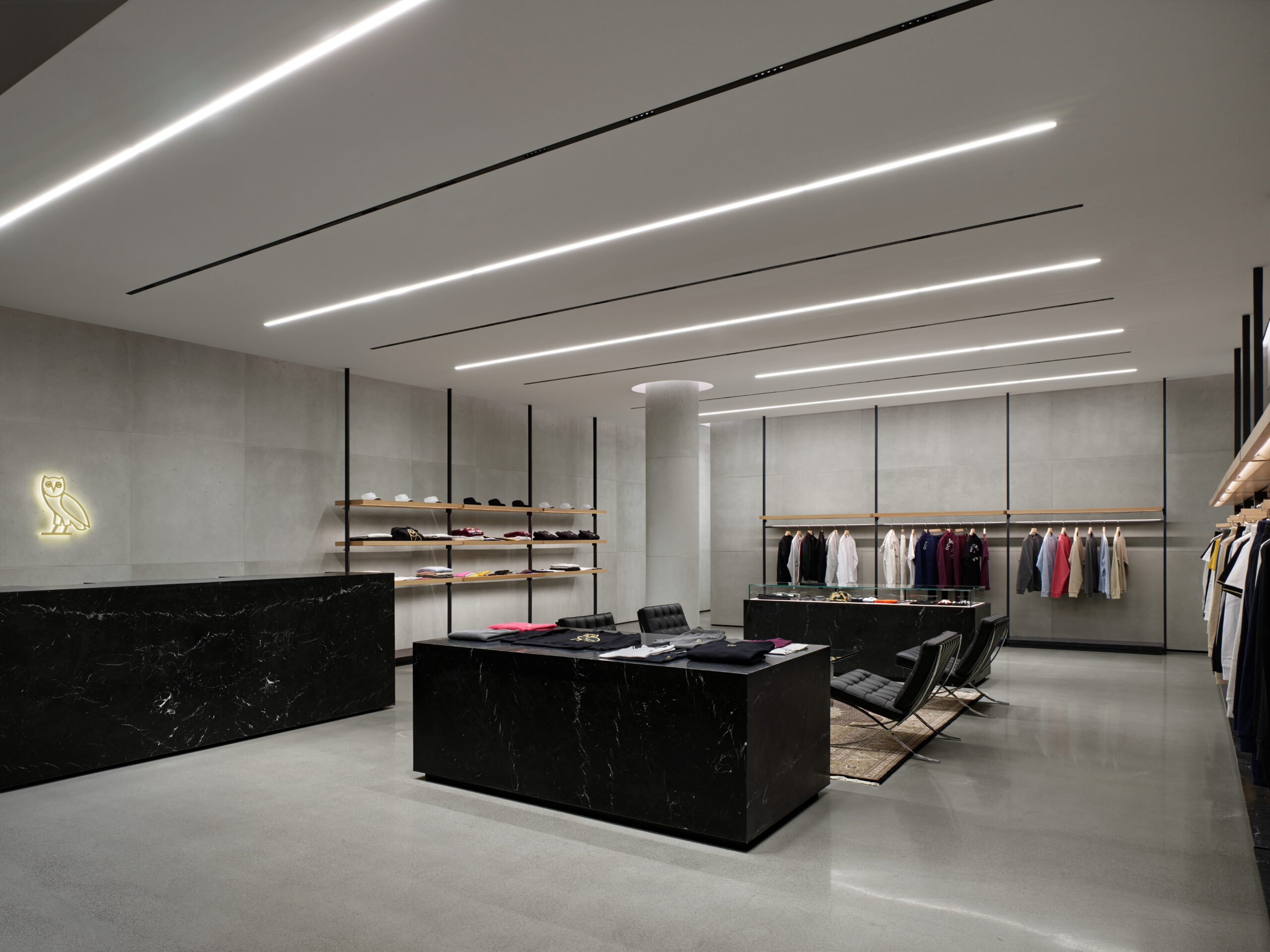 A Modern retail space, concrete cladding, concrete flooring, OVO logo, sleek black desk and clothing displays. 