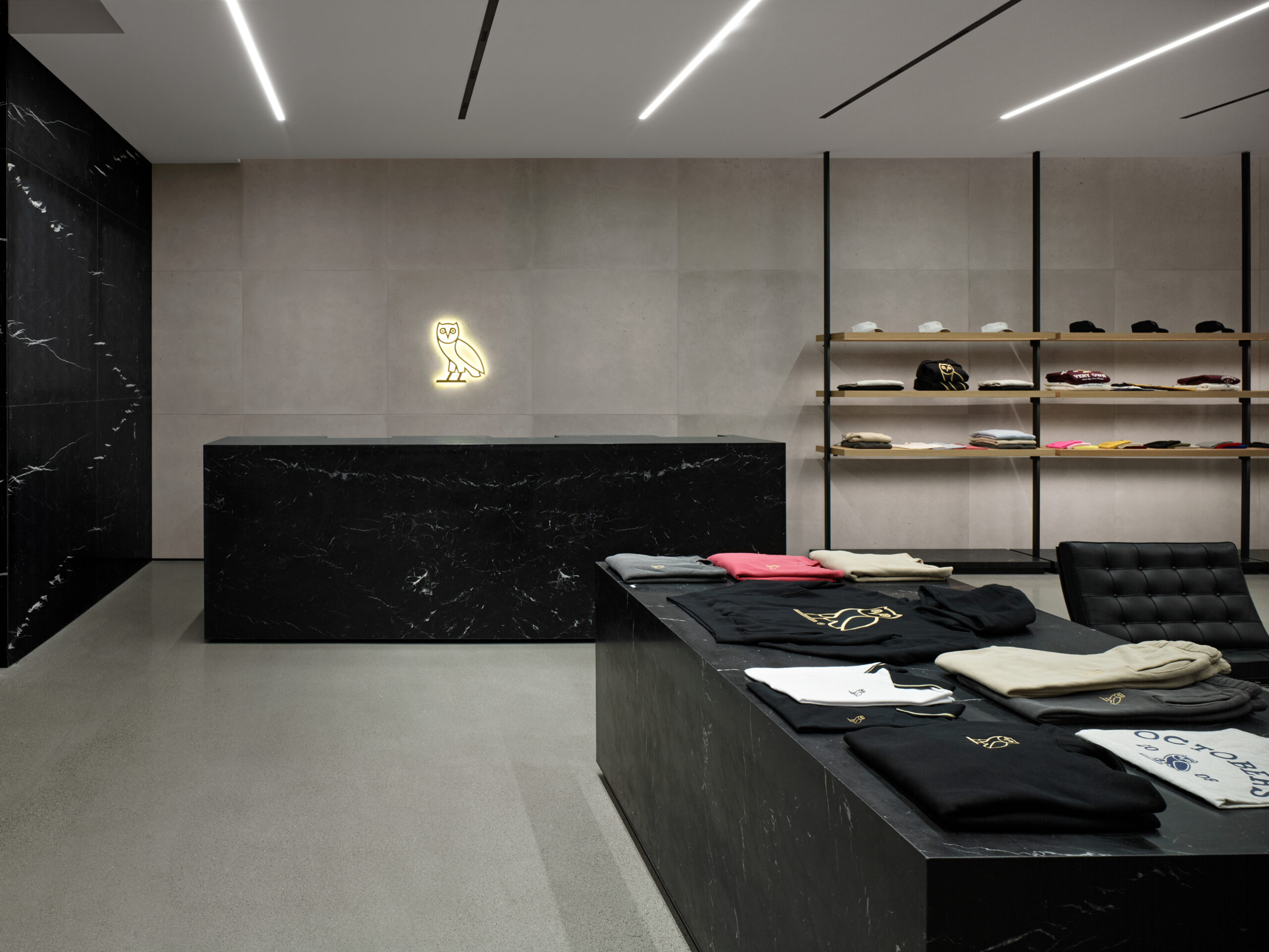 Sleek black counter with OVO logo in a modern retail space with concrete cladding and clothing display shelves.