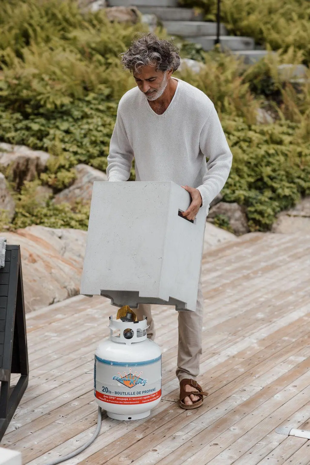 A man covering a propane tank connected to a concrete fire pit.