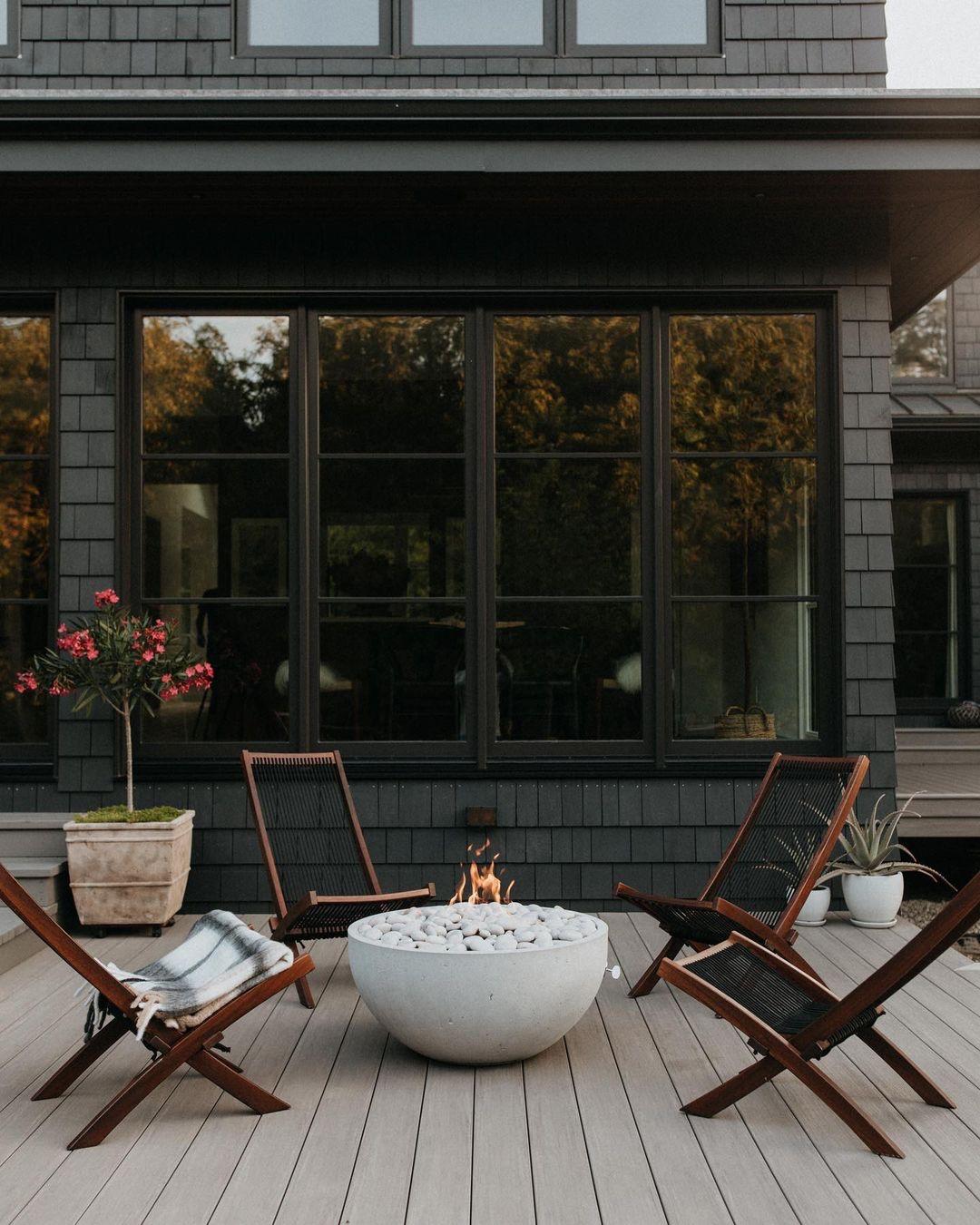 Four chairs are surrounding a bowl-shaped fire pit that is located on a back porch.