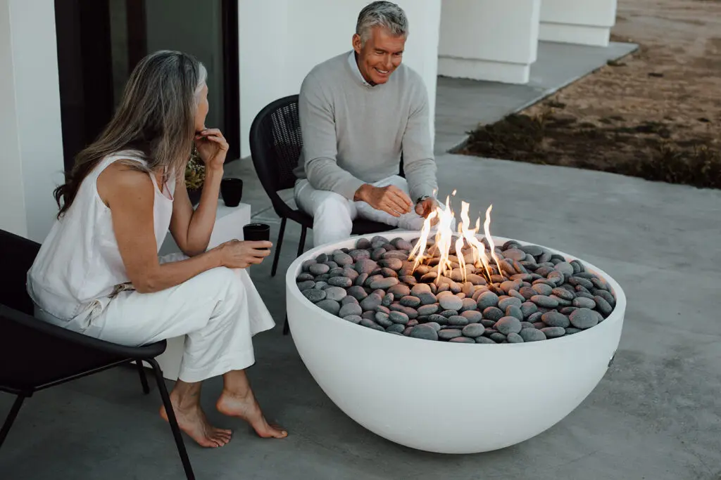 Older couple, sitting drinking coffee around a circular concrete fire pit.