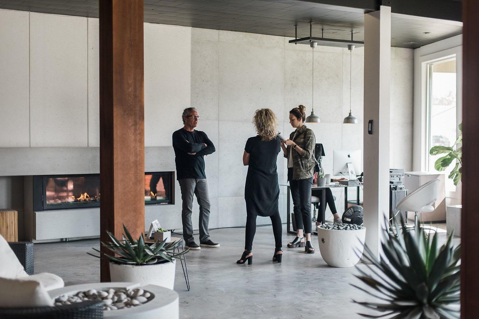 A group of three people is standing in a room with lightweight concrete cladding in the background near a fireplace.