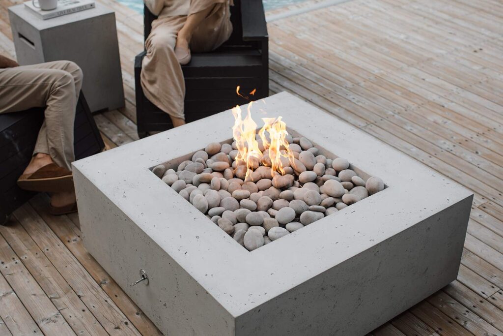 Modern outdoor fire pit with a sleek concrete design and river stones, set on a wooden deck, perfect for cozy gatherings. 